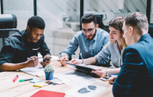 Group of diversity people searching information for provide ideas in new startup project using touch pad during brainstorming, collaboration and cooperation. Four colleagues sharing opinions at meeting